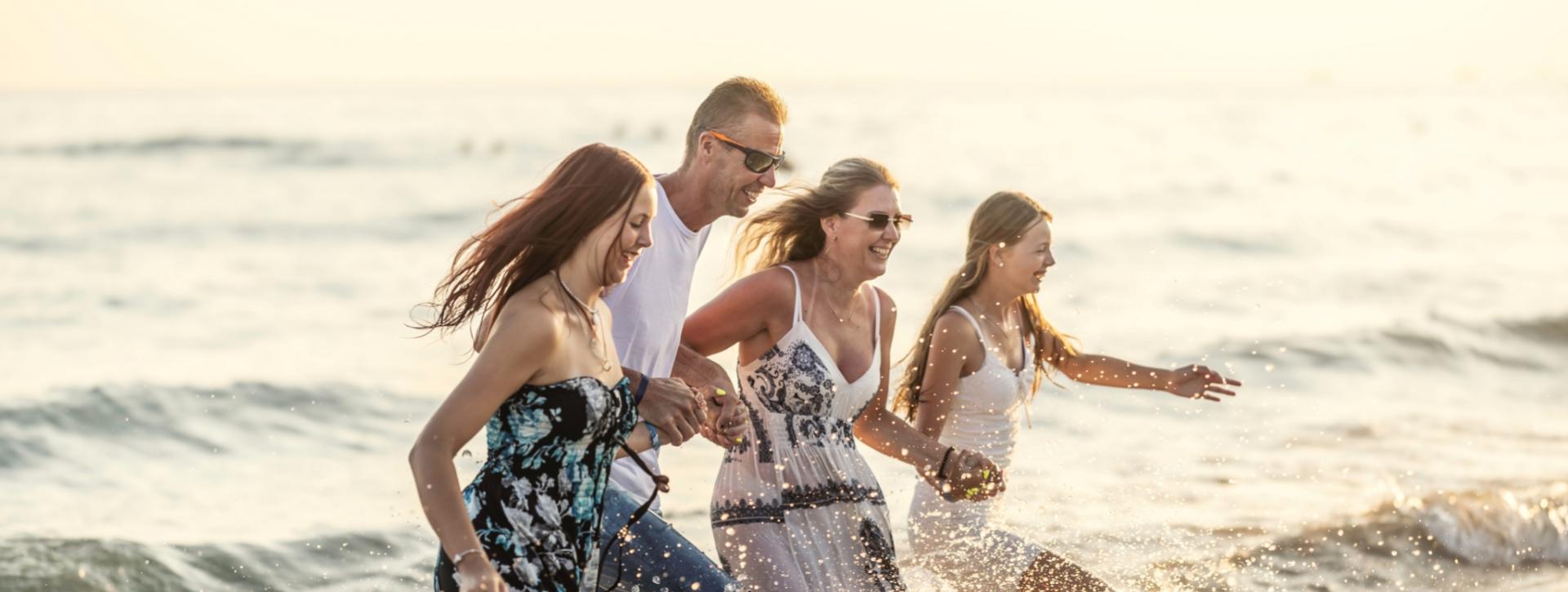 Famiglia felice corre sulla spiaggia al tramonto, spruzzi d'acqua e sorrisi.