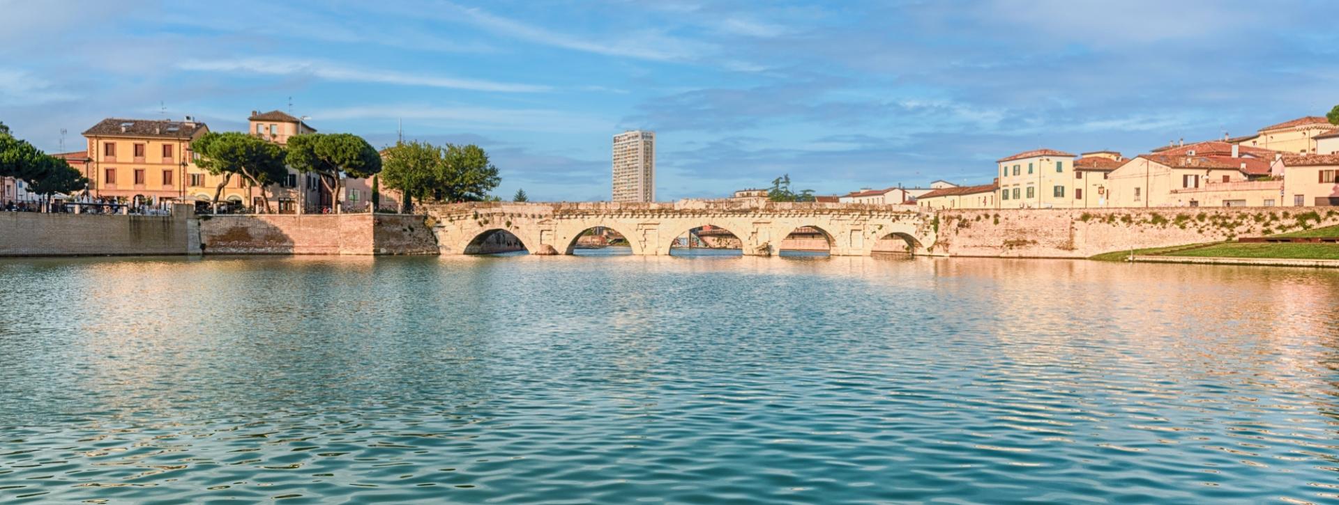 Ponte storico sull'acqua, circondato da edifici e un cielo sereno.