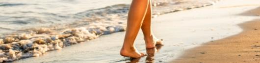 Piedi camminano sulla spiaggia, lambiti dalle onde del mare al tramonto.