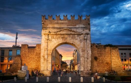 Arco romano al tramonto, con cielo nuvoloso e architettura antica in pietra.