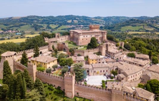 Vista aerea di un castello medievale circondato da mura e colline verdi.