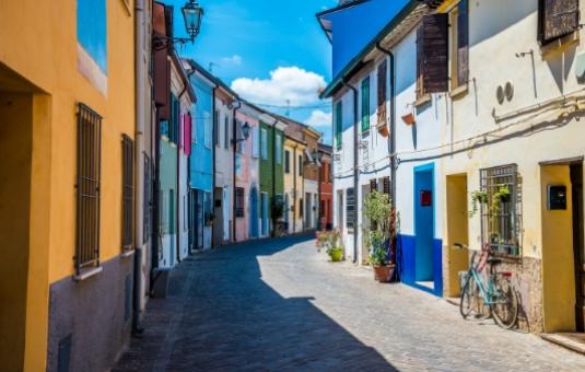 Strada pittoresca con case colorate e biciclette appoggiate ai muri, cielo sereno.