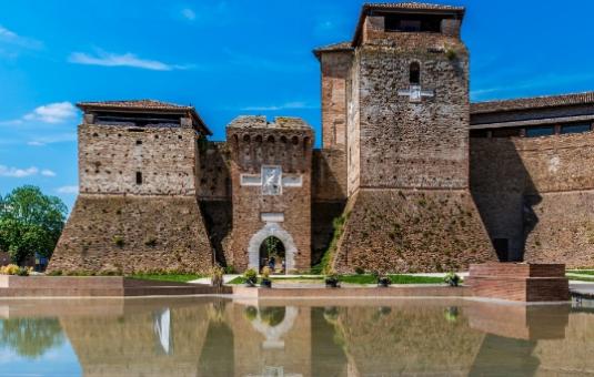 Ancient castle with reflective moat, blue sky.