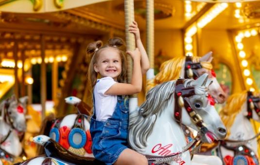 Bambina felice su una giostra colorata, sorridente mentre cavalca un cavallo bianco.