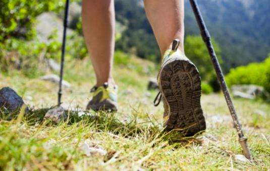 Persona cammina con bastoncini da trekking su un sentiero di montagna.