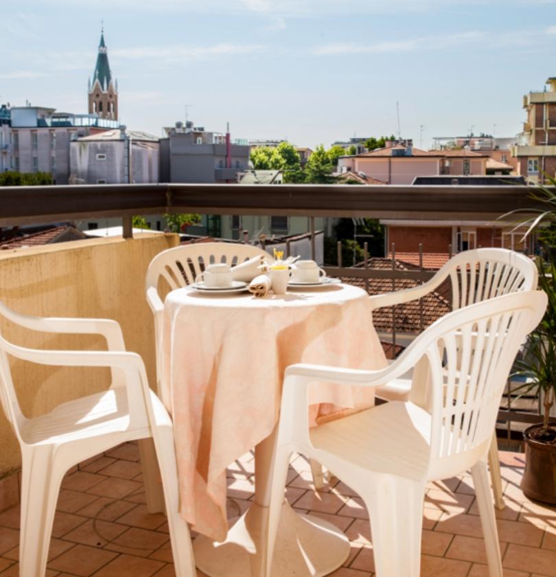 Terrazza con tavolo apparecchiato, sedie bianche e vista su edifici e campanile.