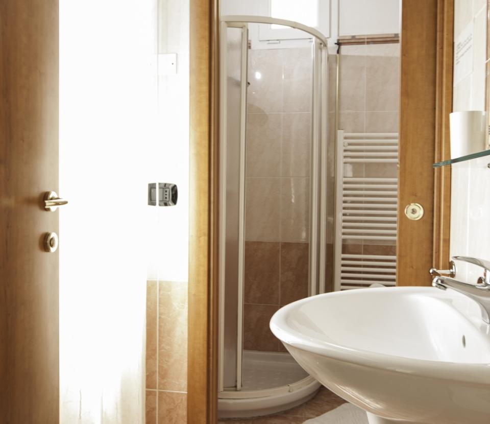 Bagno moderno con doccia, lavabo, porta in legno e piastrelle chiare.