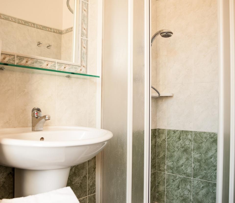 Bagno con doccia angolare, lavabo e asciugamani bianchi su pavimento piastrellato verde.