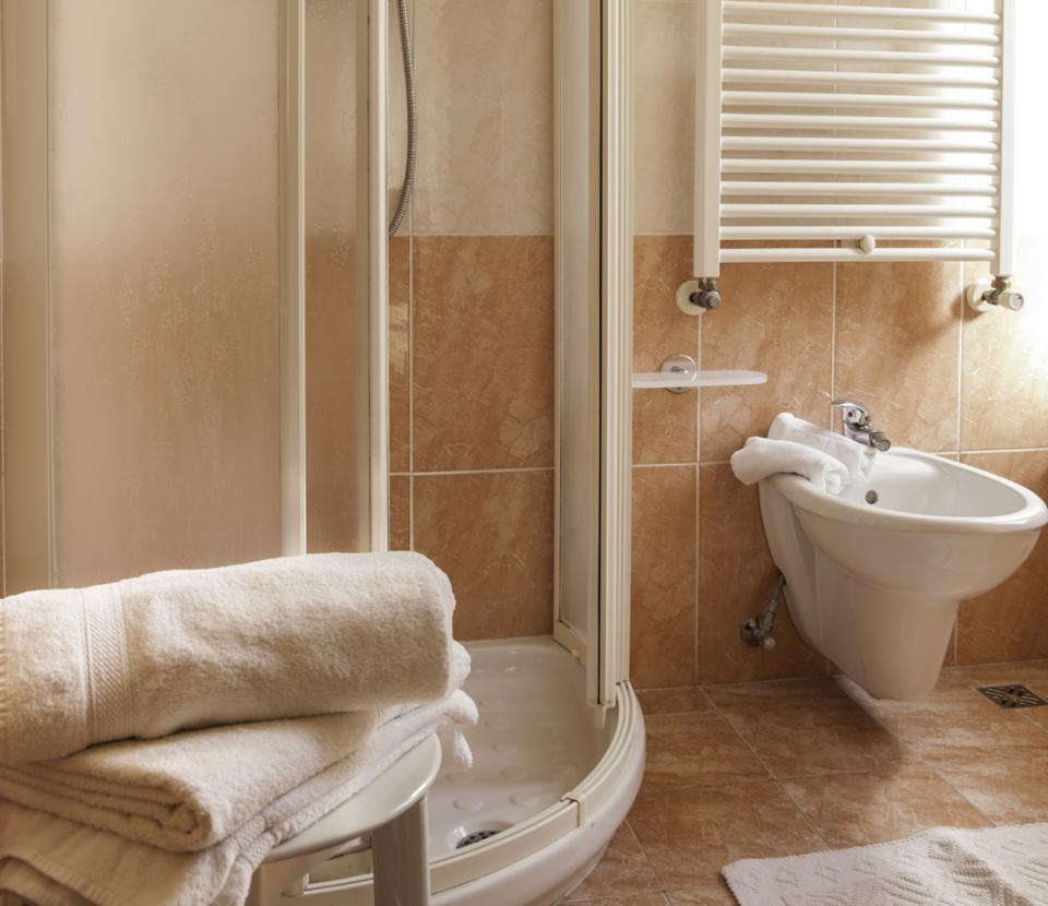 Bagno con doccia, bidet, asciugamani piegati e piastrelle beige e marroni.