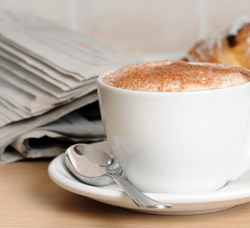 Tasse Cappuccino mit Croissant und Zeitung auf dem Tisch.