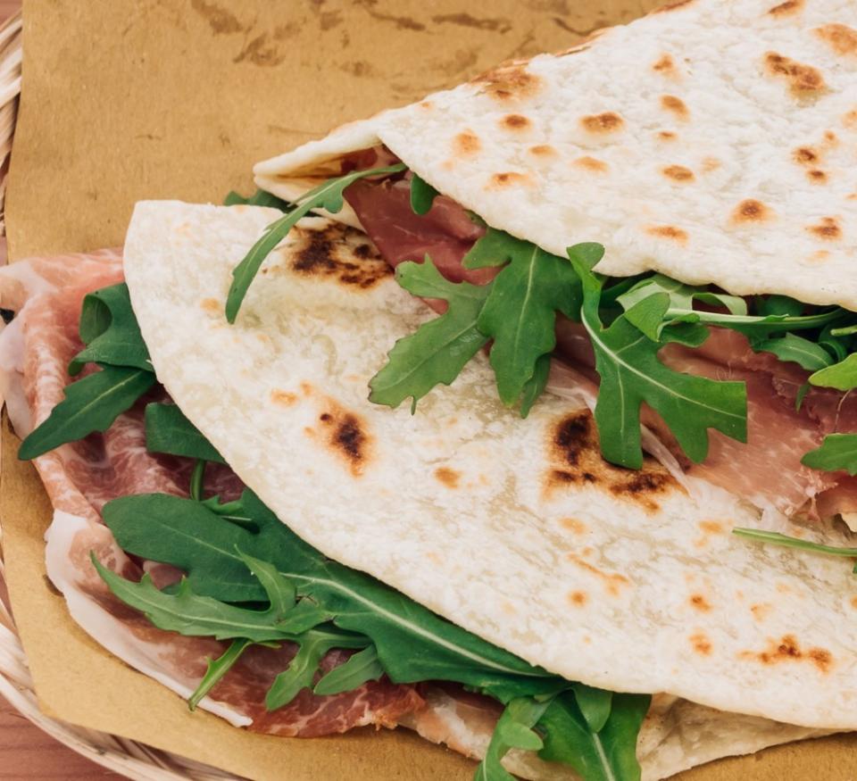 Piadina mit Schinken und Rucola auf braunem Papier.